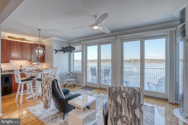 living room featuring ceiling fan with notable chandelier, a water view, light hardwood / wood-style flooring, and crown molding