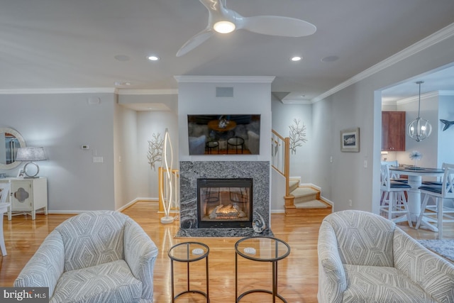 living room featuring ceiling fan, light hardwood / wood-style flooring, a high end fireplace, and ornamental molding