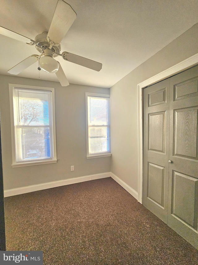 unfurnished bedroom with dark colored carpet, a closet, and ceiling fan