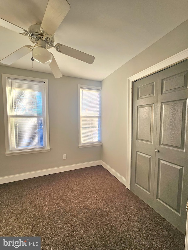 unfurnished bedroom with dark colored carpet, ceiling fan, and a closet