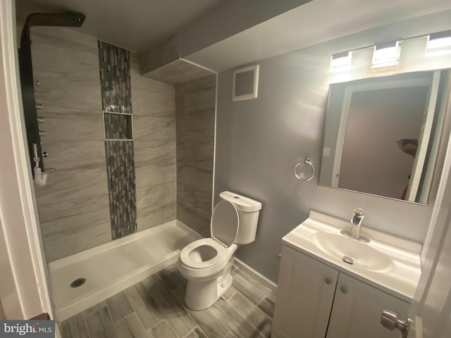 bathroom with tiled shower, vanity, and toilet