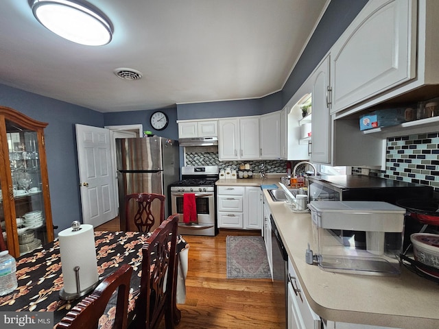 kitchen with under cabinet range hood, stainless steel appliances, a sink, visible vents, and white cabinets