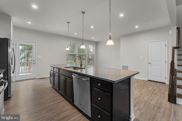 kitchen with an island with sink, stainless steel appliances, pendant lighting, light hardwood / wood-style flooring, and sink