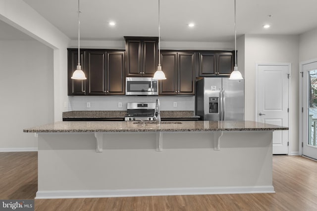 kitchen with decorative light fixtures, a breakfast bar, appliances with stainless steel finishes, and a kitchen island with sink