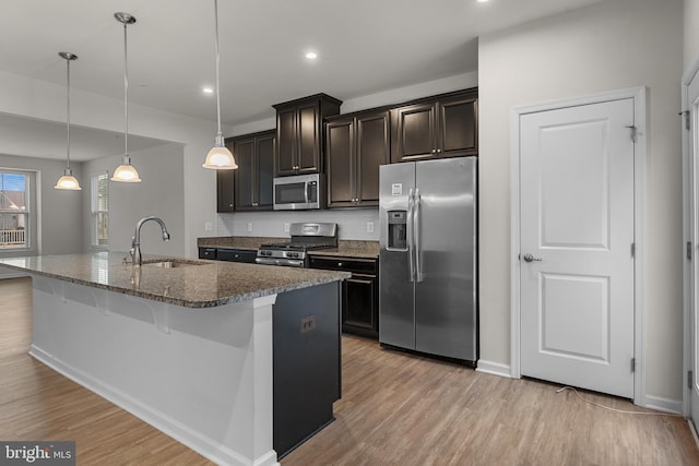 kitchen featuring decorative light fixtures, dark stone countertops, sink, a kitchen island with sink, and appliances with stainless steel finishes