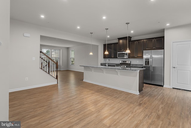 kitchen featuring appliances with stainless steel finishes, a kitchen island with sink, hanging light fixtures, stone counters, and sink