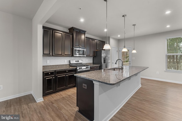 kitchen with appliances with stainless steel finishes, backsplash, a kitchen island with sink, pendant lighting, and sink