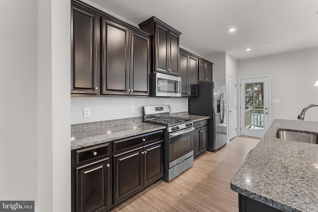 kitchen featuring decorative backsplash, sink, light wood-type flooring, appliances with stainless steel finishes, and light stone counters