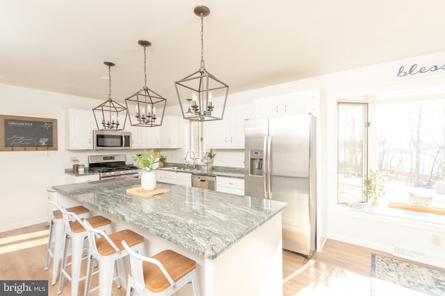 kitchen featuring light stone countertops, white cabinets, appliances with stainless steel finishes, decorative light fixtures, and light hardwood / wood-style floors