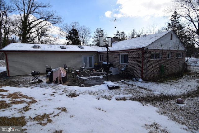 snow covered property with brick siding and french doors