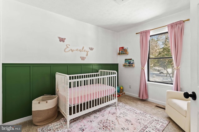 bedroom featuring a textured ceiling, light colored carpet, and a nursery area