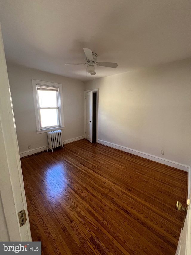 spare room featuring radiator, ceiling fan, and dark wood-type flooring