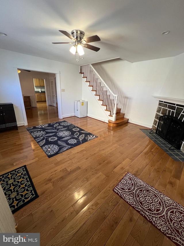 living room featuring ceiling fan, a stone fireplace, and wood-type flooring