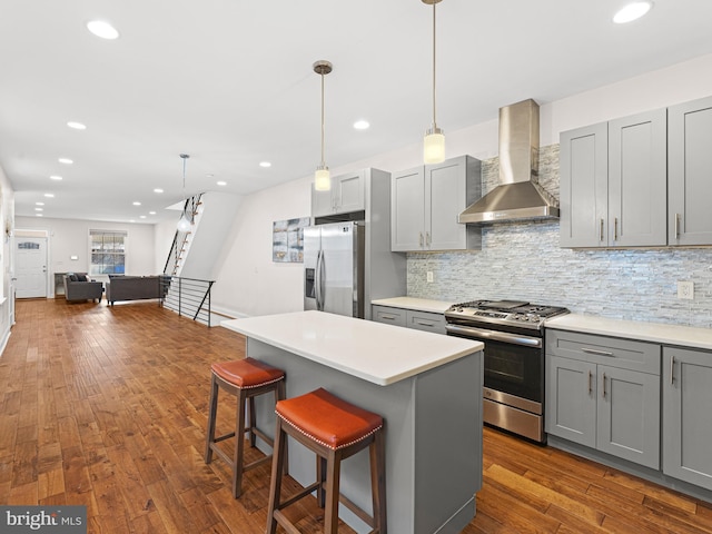 kitchen with gray cabinets, pendant lighting, stainless steel appliances, and wall chimney range hood