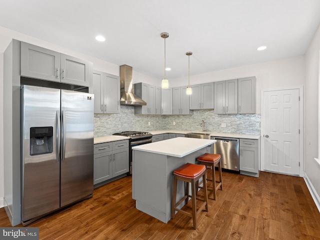 kitchen with a center island, wall chimney exhaust hood, stainless steel appliances, sink, and decorative light fixtures