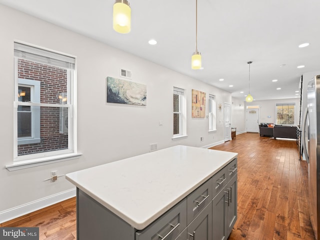 kitchen featuring dark hardwood / wood-style flooring, decorative light fixtures, a center island, gray cabinets, and stainless steel refrigerator