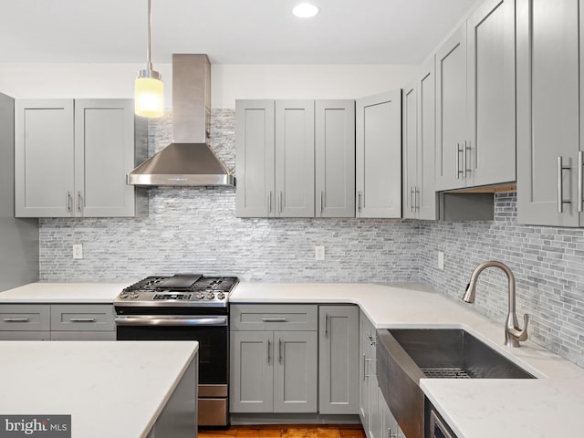 kitchen featuring gray cabinetry, wall chimney range hood, stainless steel gas range, backsplash, and pendant lighting