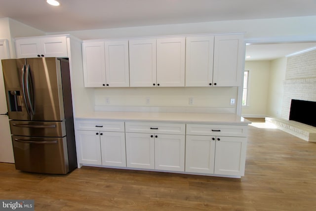 kitchen with white cabinetry, stainless steel fridge, light hardwood / wood-style flooring, and a brick fireplace