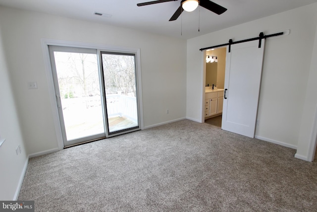 carpeted empty room featuring a barn door, ceiling fan, and sink