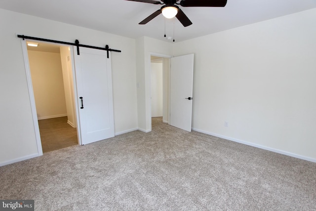 unfurnished bedroom featuring a barn door, light colored carpet, and ceiling fan