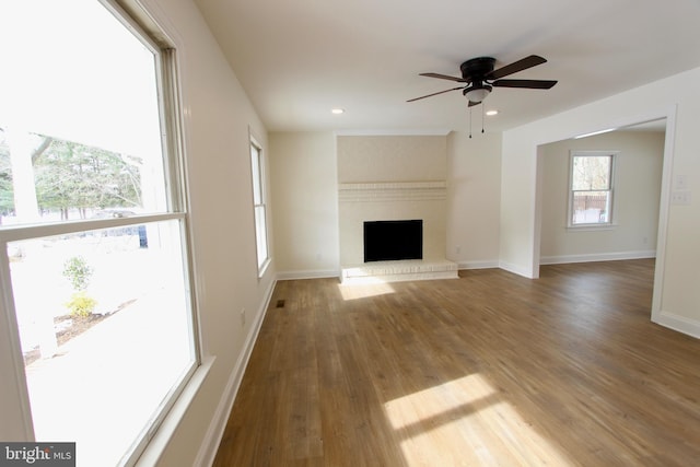 unfurnished living room featuring ceiling fan, wood-type flooring, and a brick fireplace