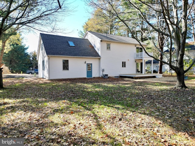 rear view of property featuring a yard, a balcony, and a wooden deck