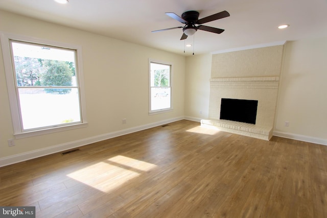 unfurnished living room with hardwood / wood-style flooring, ceiling fan, and a brick fireplace