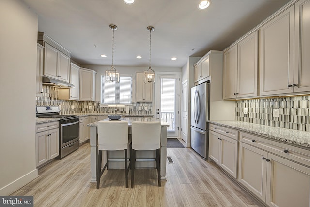 kitchen featuring decorative light fixtures, light stone countertops, appliances with stainless steel finishes, and a breakfast bar area