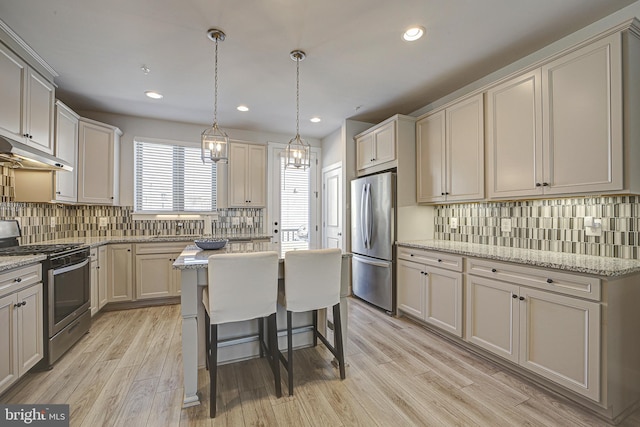 kitchen featuring stainless steel appliances, light stone counters, a kitchen breakfast bar, light hardwood / wood-style floors, and a kitchen island