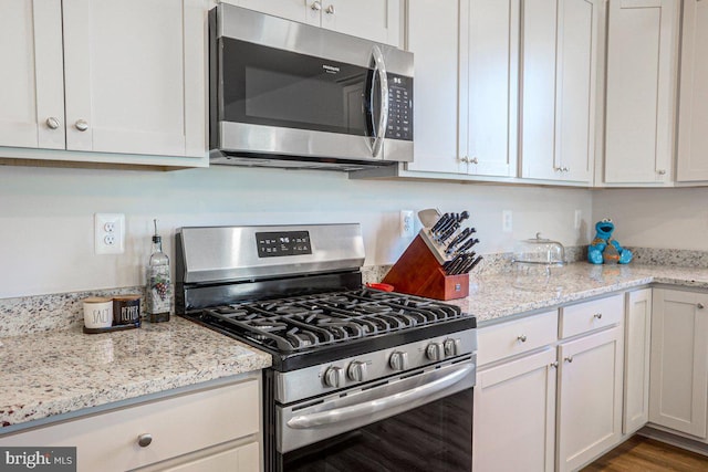 kitchen with white cabinets, stainless steel appliances, and light stone countertops