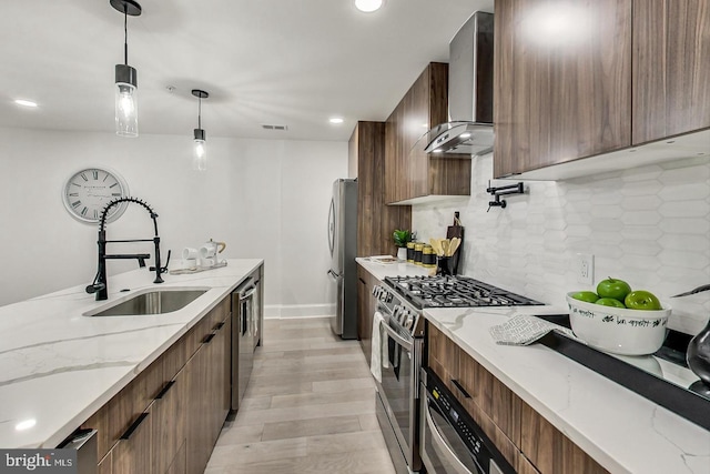 kitchen featuring light stone counters, wall chimney range hood, sink, and appliances with stainless steel finishes