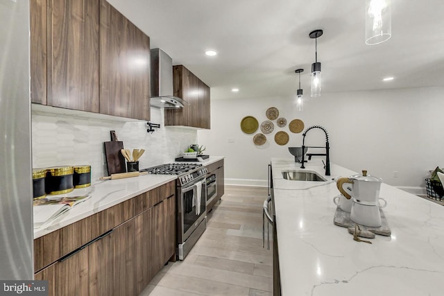 kitchen with sink, hanging light fixtures, wall chimney exhaust hood, light stone countertops, and gas stove