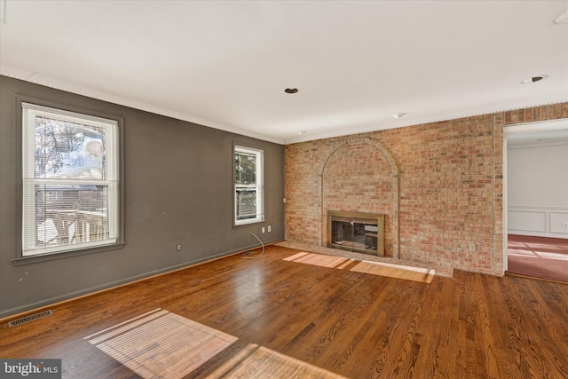 unfurnished living room with brick wall, plenty of natural light, and hardwood / wood-style floors