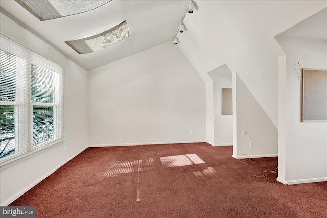 interior space featuring rail lighting, vaulted ceiling, and dark colored carpet