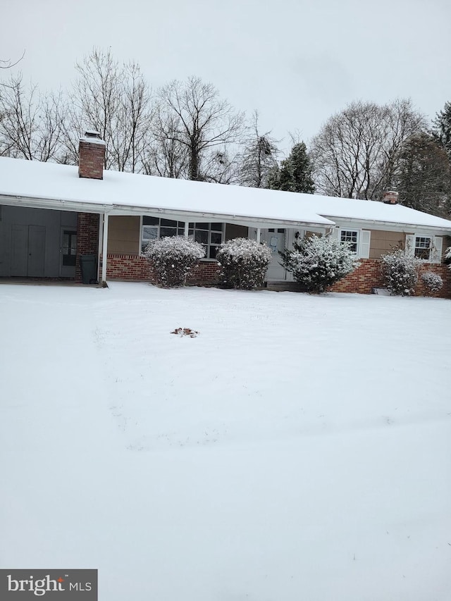 view of snowy exterior featuring brick siding and a chimney