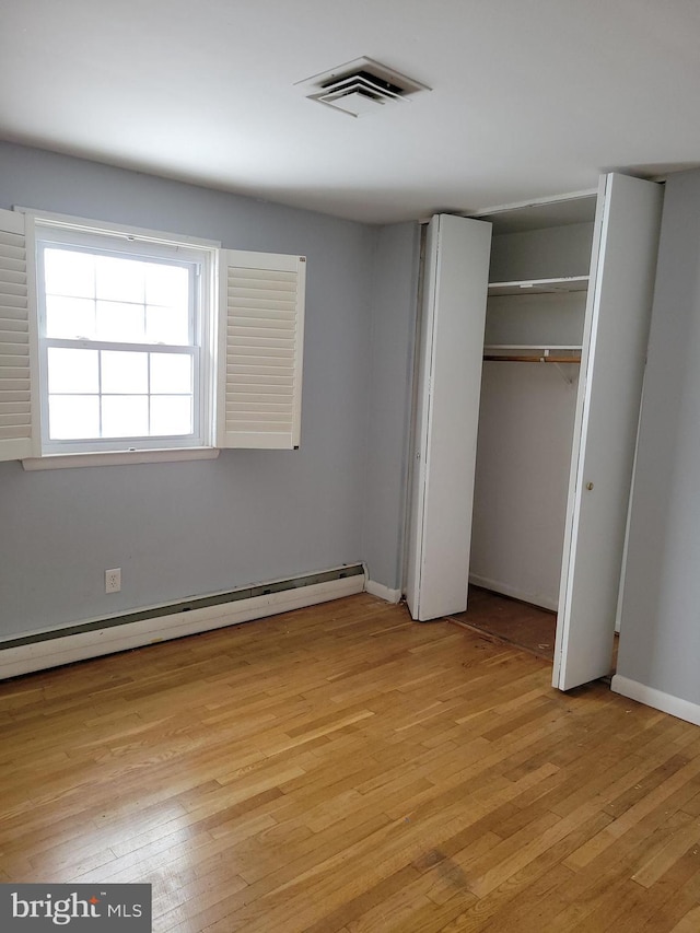 unfurnished bedroom with light wood finished floors, visible vents, a closet, and a baseboard radiator