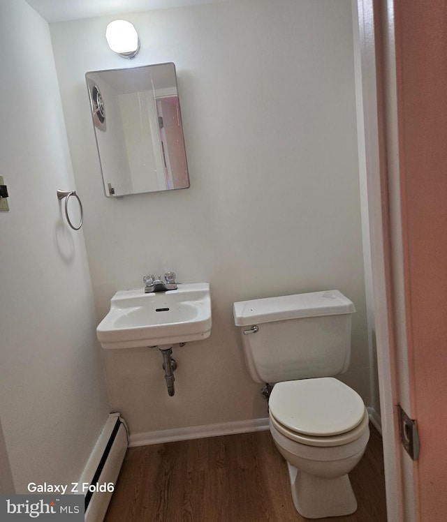 half bathroom with wood finished floors, baseboards, a sink, a baseboard heating unit, and toilet