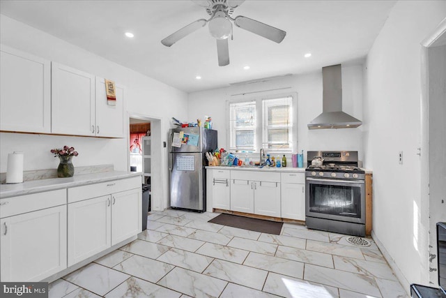 kitchen featuring stainless steel appliances, ceiling fan, sink, white cabinetry, and wall chimney range hood