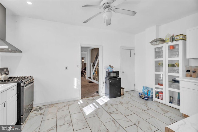 kitchen with white cabinets, ceiling fan, wall chimney range hood, and gas range