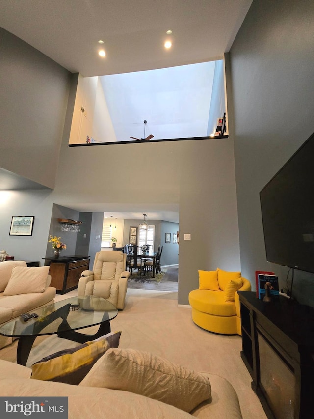 living room featuring a towering ceiling, light colored carpet, and ceiling fan