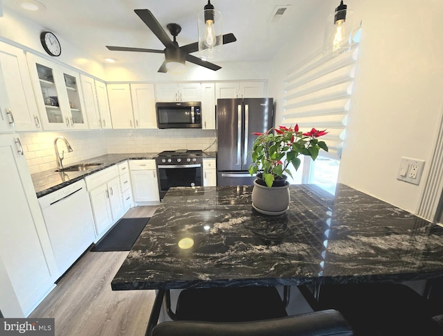 kitchen featuring white cabinetry, sink, dark stone counters, decorative backsplash, and appliances with stainless steel finishes