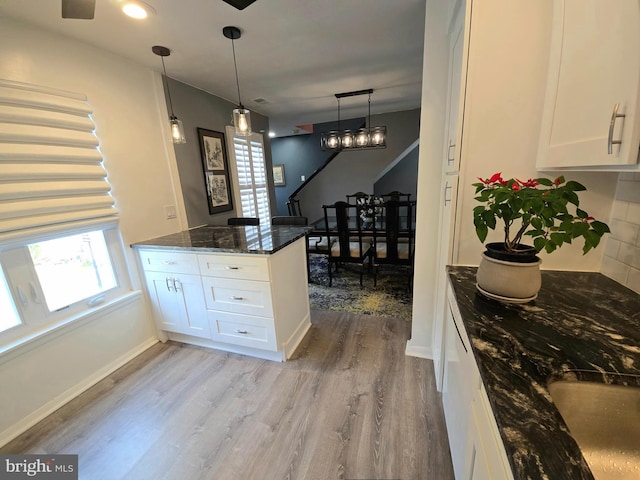 kitchen featuring dark stone countertops, white cabinetry, light hardwood / wood-style floors, and decorative light fixtures