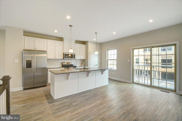 kitchen featuring decorative light fixtures, an island with sink, white cabinets, and appliances with stainless steel finishes