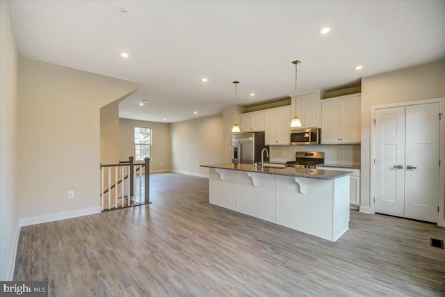 kitchen with a breakfast bar, a kitchen island with sink, white cabinetry, stainless steel appliances, and light hardwood / wood-style floors