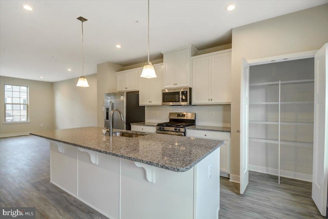 kitchen with sink, dark stone countertops, stainless steel appliances, white cabinets, and decorative light fixtures