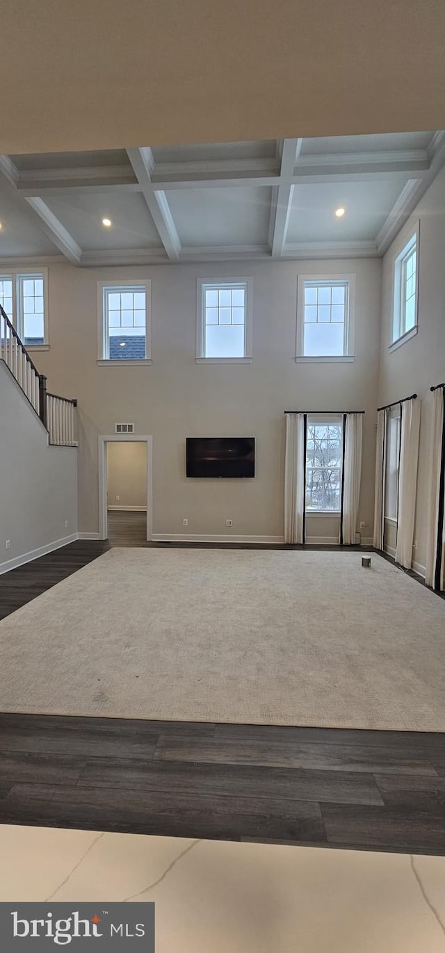 unfurnished living room featuring a towering ceiling, coffered ceiling, hardwood / wood-style floors, and beam ceiling