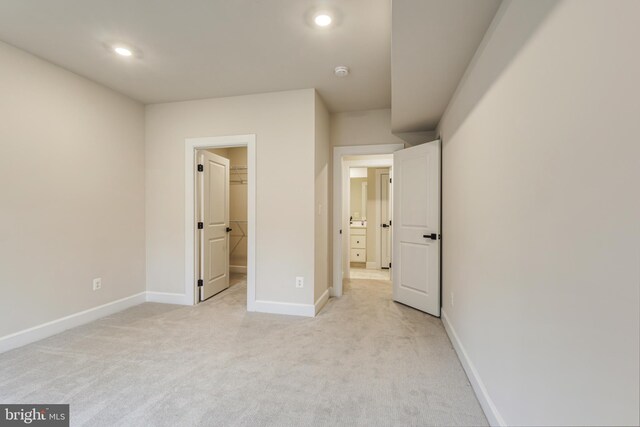 unfurnished bedroom with a walk in closet and light carpet