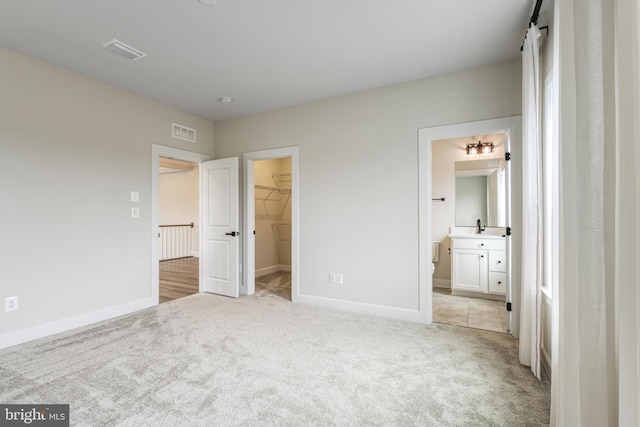 unfurnished bedroom featuring connected bathroom, sink, a walk in closet, light carpet, and a closet