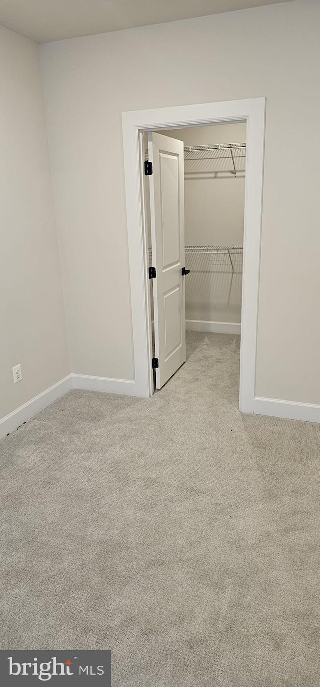 unfurnished bedroom with light colored carpet and a walk in closet