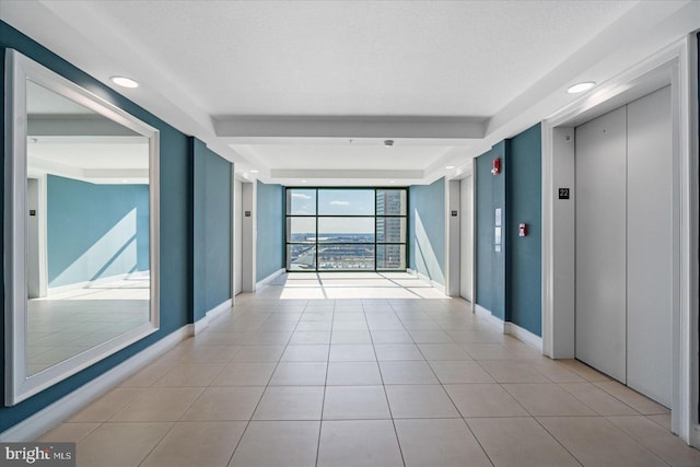 hall with light tile patterned floors, a textured ceiling, a wall of windows, and elevator